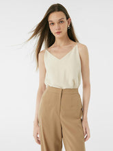 A woman wears a white camisole top.